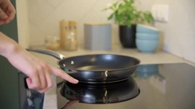 Kadın eli mutfaktaki modern indüksiyon sobasını açıyor.