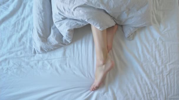 Jambes féminines dans le lit sous la couverture — Video