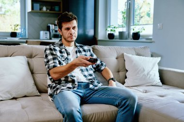 Adam kanepede oturup televizyon izliyor, uzaktan kumandayı kullanarak kanal değiştiriyor. Evde dinlenmek, hafta sonları dinlenmek.