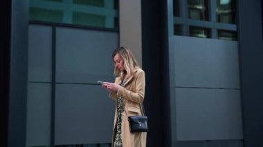 Kadın caddede yürüyor ve akıllı telefon kullanıyor.