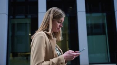 Kadın caddede yürüyor ve akıllı telefon kullanıyor.