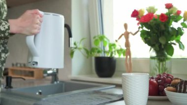 Kadın musluktan suyu mutfakta elektrikli su ısıtıcısına döküyor.