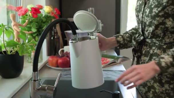 Vrouw gieten water uit kraan in elektrische waterkoker in de keuken — Stockvideo