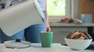 Çay demlemek için çaydanlıktan su döken kadın.