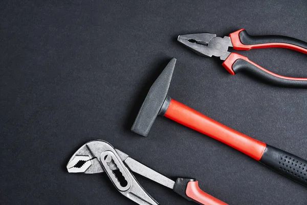 Yenileme aletleri. Tamir ve bakım ekipmanları. Siyah zemin üzerinde çekiç, İngiliz anahtarı ve maşa, üst görünüm düz yatıyordu