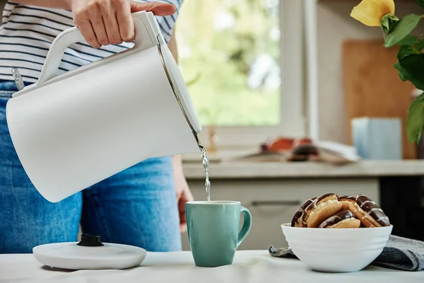 Çay zamanı, çay hazırlamak için elektrikli çaydanlıktan kaynamış su döken kadın, mutfakta sabah kahvaltısı.
