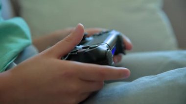 Çocuk oturma odasında kanepede oturuyor ve elinde oyun konsoluyla video oyunu oynuyor. Çevrimiçi eğlence ve eğlence aktivitesi.