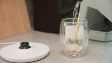 Çay yapmak, elektrikli çaydanlıktan akan sıcak su çay poşeti ve kaşıkla cam bardağa doluyor.