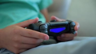 Çocuk oturma odasında kanepede oturuyor ve elinde oyun konsoluyla video oyunu oynuyor. Çevrimiçi eğlence ve eğlence aktivitesi.