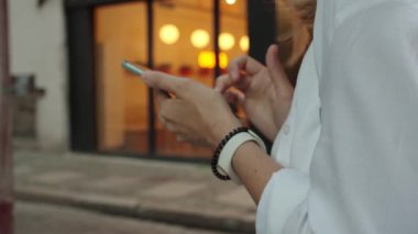 Woman using smartphone at evening street with blurred lights, Female typing message, browsing internet while walking at city.