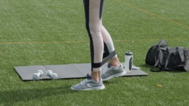 Yeşil çimenlerde elastik olgun bantla egzersiz yapan kadın bacaklar, açık havada spor yapan kadın antrenman, sağlıklı yaşam tarzı kavramına uygunluk.