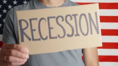 USA economic crisis, recession and and inflation, Man shows paper sheet with word recession against USA flag, Rising prices for consumer goods and services