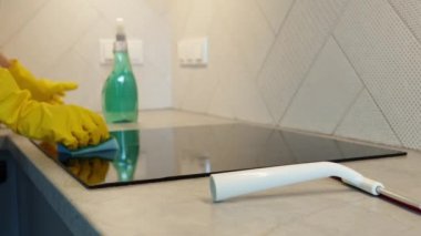 Woman in yellow rubber gloves cleans kitchen induction hob with cleaning spray and sponge. Clear kitchen appliance, Daily chores and housework