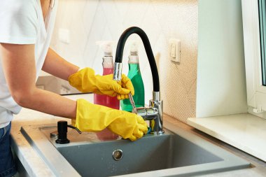 Woman cleaning water tap at sink in the kitchen
