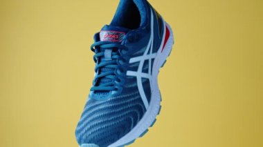 Flying Asics Gel Nimbus shoes on yellow background, Creative shot of Asics sport sneakers for jogging