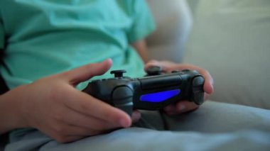 Çocuk oturma odasında kanepede oturuyor ve elinde oyun konsoluyla video oyunu oynuyor. Çevrimiçi eğlence ve eğlence aktivitesi.