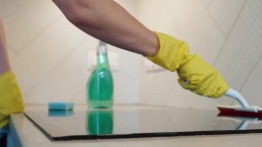 Woman in yellow rubber gloves cleans kitchen induction hob with cleaning spray and sponge. Clear kitchen appliance, Daily chores and housework