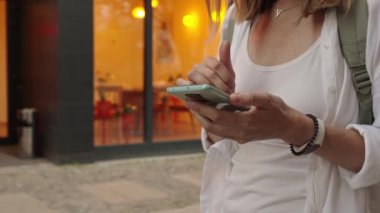 Woman using smartphone at evening street, Female typing message, browsing internet while walking at city.