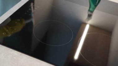 Woman in yellow rubber gloves cleans kitchen induction hob with cleaning spray and sponge. Clear kitchen appliance, Daily chores and housework