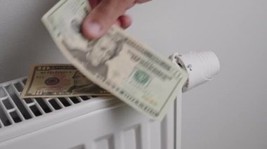 Counting dollar bills near heating radiator, Energy crisis concept, Rising costs in private households for gas bill due to inflation and war