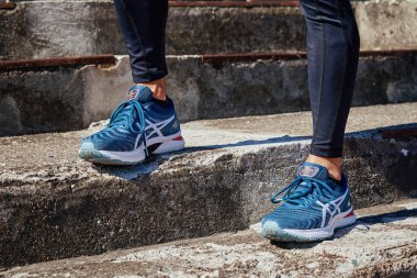 Male sprinter wearing Asics Gel Nimbus at concrete stairs background. Sport and fitness runner athlete training at stadium. Katy Wroclawskie, Poland - August 07, 2022