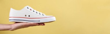 Sarı arka planda kadın eli spor ayakkabıları, gündelik moda ayakkabılar yakın plan, kopya alanı olan yaratıcı minimal tasarım