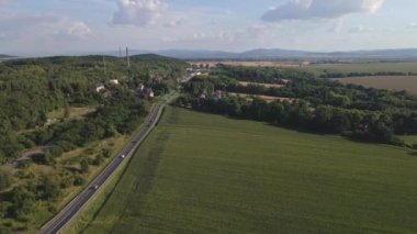 Aerial view of rural road with car moving along it. Car traffic on countryside highway near small village and mountain background