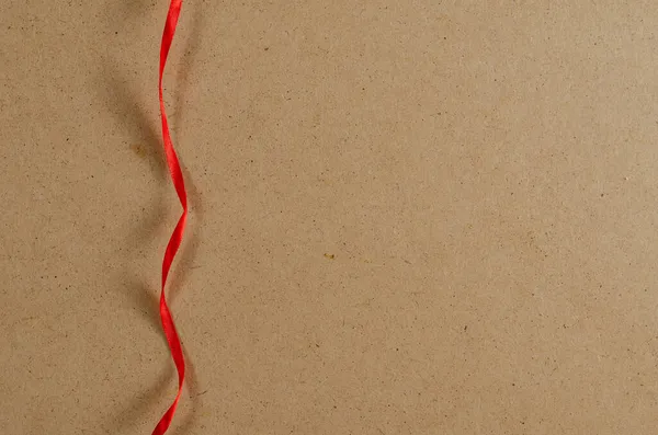 Una delgada cinta roja verticalmente sobre el fondo marrón. —  Fotos de Stock