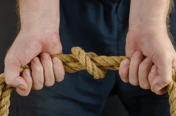 Adult Male tightens the knot on the rope. Hands hold a yellow jute rope horizontally. Close-up. Selective Focus.