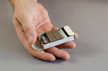 El ve zımba kutusu gri arka planda. Zımba niyetine metal zımba zımbalı kağıt kutu tutan adam. Dizinin bir parçası. Yakın plan. Seçici odak.