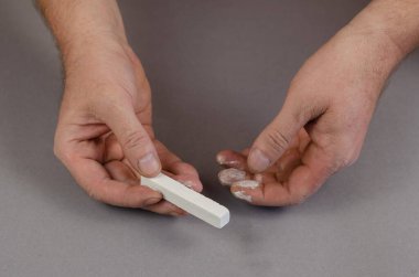 Gri arka planda iki el ve bir parça beyaz tebeşir. Dikdörtgen şeklinde tebeşir tutan bir adam. Seçici odak.