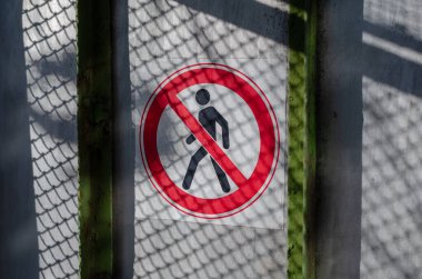 Çitlere erişimi yasaklayan bir işaret. Kırmızı ve beyaz yasak işareti olan gri çit. Çitin üzerindeki tel örgülerin gölgeleri.