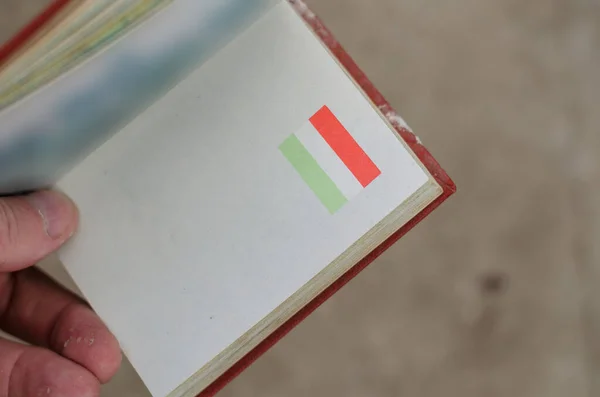 ハンガリー国旗が掲揚されたオープンブックを手に取ります 小さなハードカバーの本 肩越しの眺め 部屋の中だ 選択的フォーカス — ストック写真
