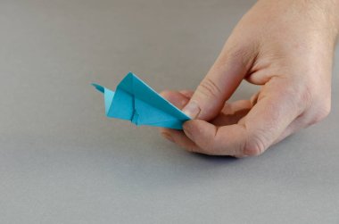 Bir adamın elinde mavi bir kağıt uçak var. Elinde origami tutan biri. Gri arka plan. Yakın plan. Seçici odak.