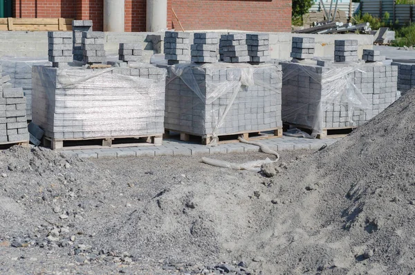 İnşaat endüstrisi, inşaat malzemeleri. Paletler dolusu gri kiremitler ve bir yığın kum. Plastik ambalaja sarılı yeni beton bloklar ve kaldırımlar. Kimse yok..