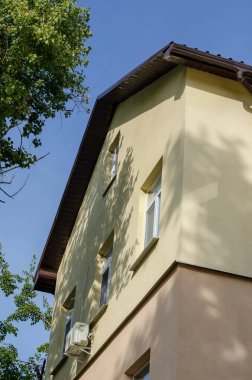 Mavi gökyüzüne karşı sarı ve pembe bir ev. Drenaj borusu olan kahverengi çatı. Düşük Açı Görünümü. Seçici Odaklanma.