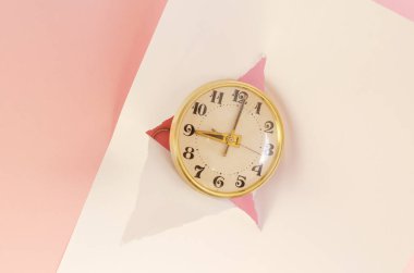 Klasik saat, beyaz gözyaşı kağıdı, pembe arka plan. Yaldızlı çerçeveli yuvarlak mekanik masa saati. Seçici odak.