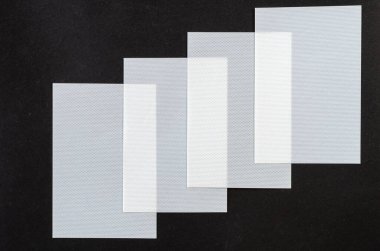 Beyaz plastik çarşaflı minimalist kompozisyon. Siyah arkaplana karşı dikdörtgen dokulu çarşaflar. Yukarıdan açılı görünüm.