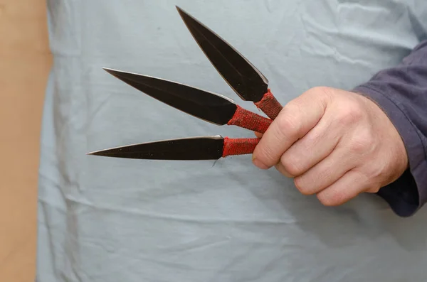 A hand with three knives. Adult male holding throwing knives.