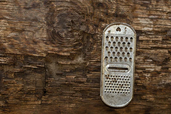 Old rusty kitchen grater on a rotting board. Top view. Copy space. Selective focus.
