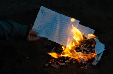 Bir kadın iş günlüğünün sayfalarını ateşe atıyor. Defterden yırtılmış sayfaları yakmak. İş belgelerini yok etmek. Alacakaranlık. Defocus, bulanıklık, gürültü, tahıl etkisi.