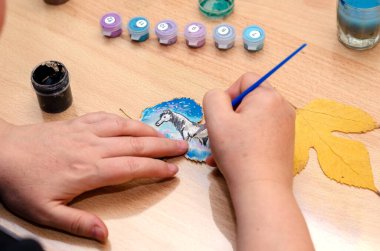 Modern sanat. Kurumuş bir ağaç yaprağına at çizen bir kadın. Onun elleri düşmüş yaprağı masanın üzerinde tutuyor. Yaratıcılık. Seçici odak.