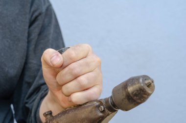 Bir adam elinde eski bir matkap tutuyor. Paslı metal bir el aleti. Yakın plan. Seçici odak.