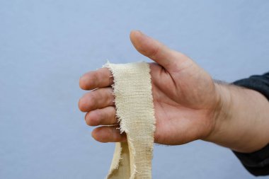 Mavi arka planda dar bir kumaş şeridi olan bir adam. Sağ kolunda yırtık pırtık bir kumaş şeridi var. Yakın plan. Seçici odak.