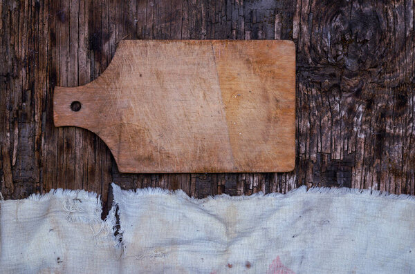 Wooden cutting board and old tattered fabric on a textured wooden background. Top view. Selected background.