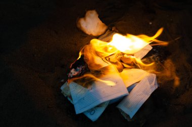 Bir kadın iş günlüğünün sayfalarını ateşe atıyor. Defterden yırtılmış sayfaları yakmak. İş belgelerini yok etmek. Alacakaranlık. Defocus, bulanıklık, gürültü, tahıl etkisi.