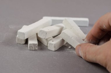 Yetişkin bir adamın eli gri arka planda yatan bir tebeşir parçasını alır. Dikdörtgen şeklinde beyaz tebeşir parçaları. Seçici odak.