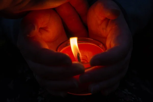 一个女人的手掌之间燃烧着的红色蜡烛 那个女人把蜡烛的火焰遮挡在外面的风中 颗粒效应 — 图库照片