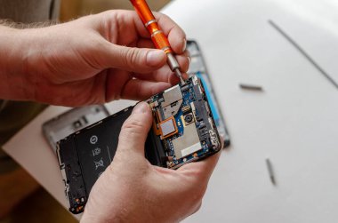 Bir adam Smartphone tamir ediyor. Eller tornavidayı tutsun ve sim kart döngüsünü kessin. Servis Tamiri. Seçici odak.
