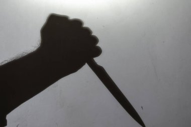 Görüntü, bulanıklık, gürültü, tahıl etkisi. Açık gri bir duvarda elinde bıçak olan bir adamın koyu renk silüeti. Kapalı alanda. Seçici odak.